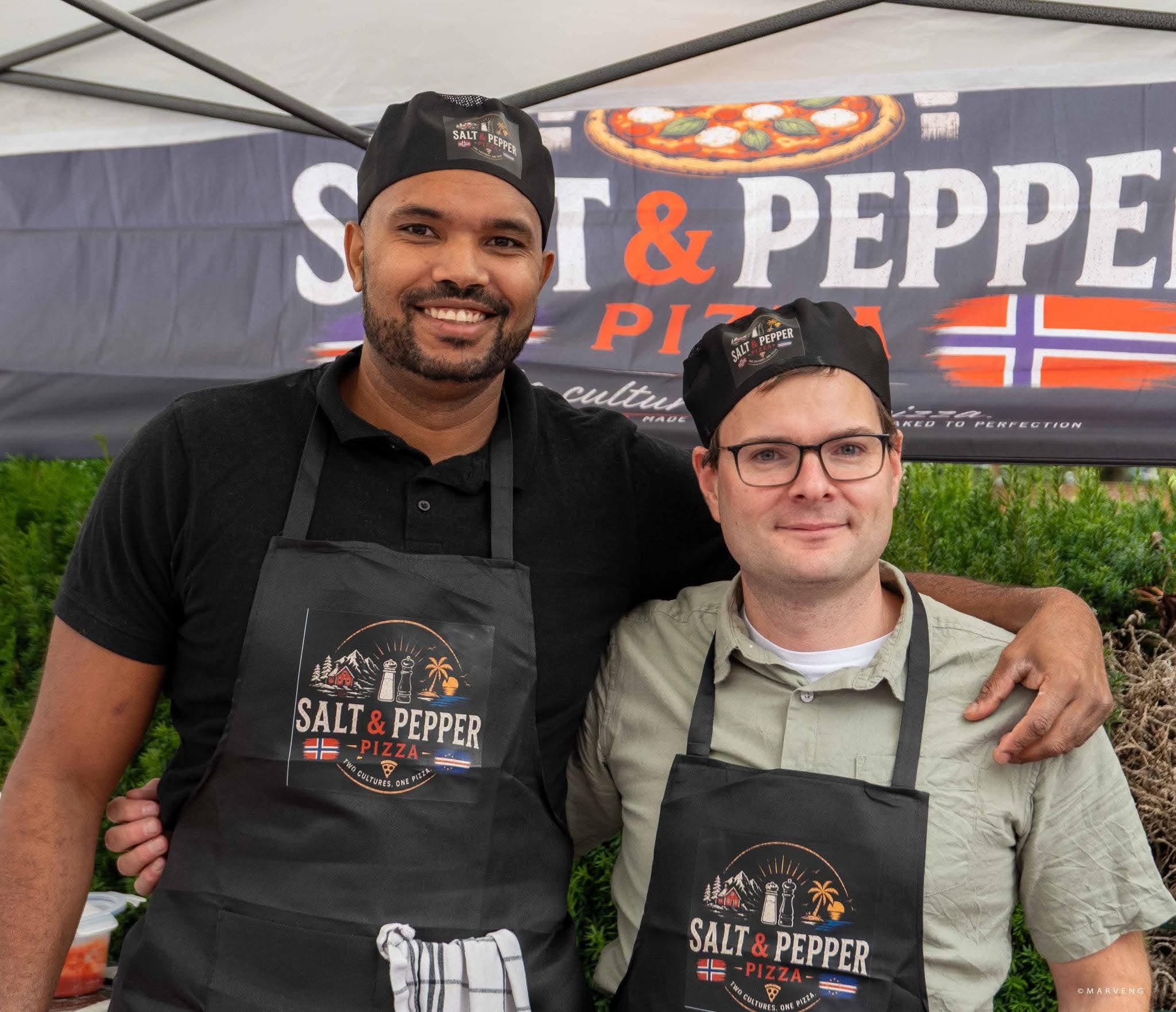 To av pizzakokkene foran Salt & Pepper Pizza-banneren